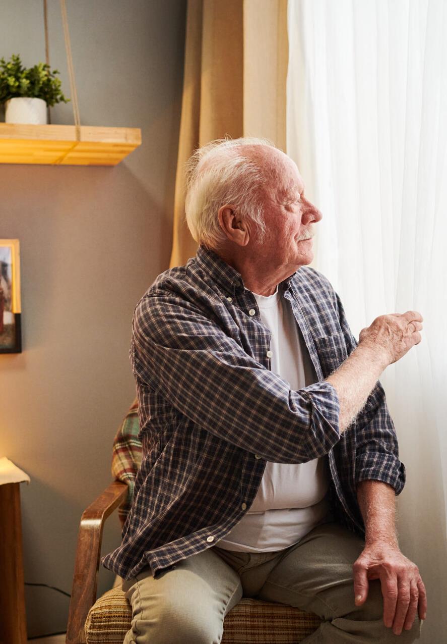 An older adult sitting near a bright window at home.