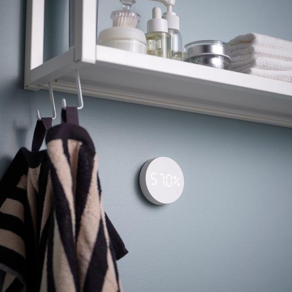 A smart thermostat installed on a wall near hanging coats.